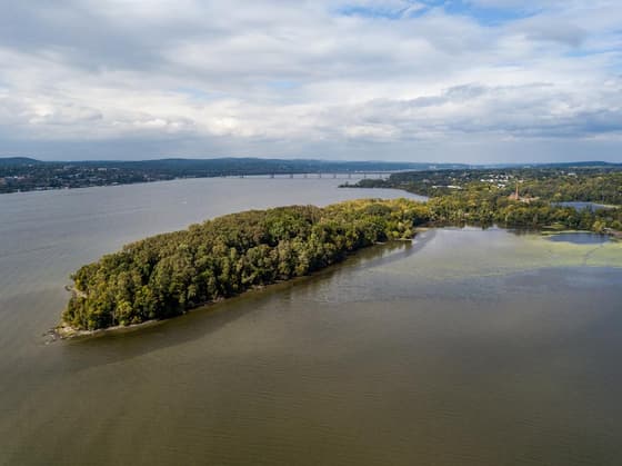 Denning's Point seen from across the water: a long low wooded peninsula reaching out into the Hudson, with the far shore and hills faint behind it under a cloudy sky.
