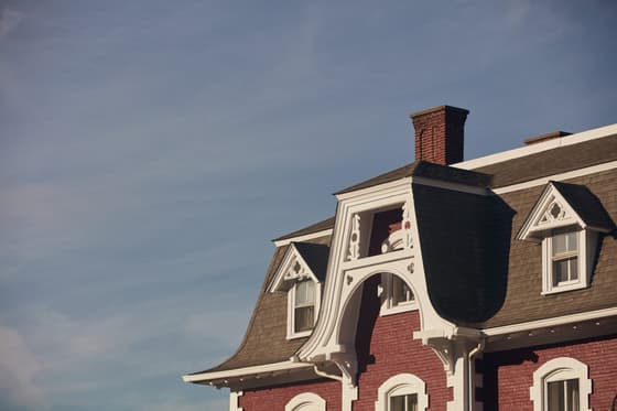 The existing Dutchess Manor building: a brick nineteenth-century house with a steep dark mansard roof, dormer windows and a heavy bracketed cornice, shot from below against a pale sky.