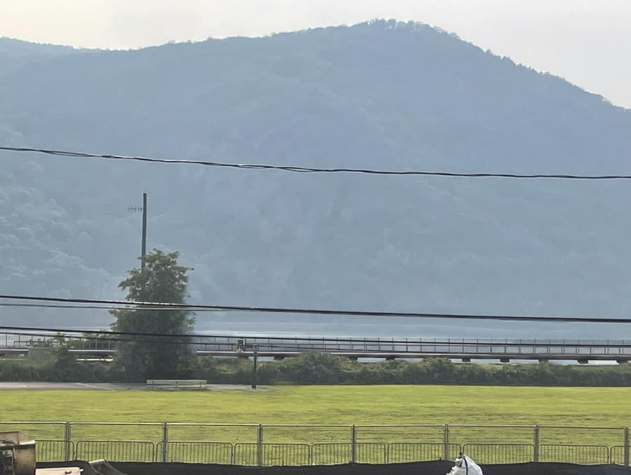 The same view west from lower Fair Street with the proposed Fjord Trail built. A low horizontal line — the elevated trail deck and its fence — runs across the middle of the frame at the shoreline, below the river and the mountain beyond.