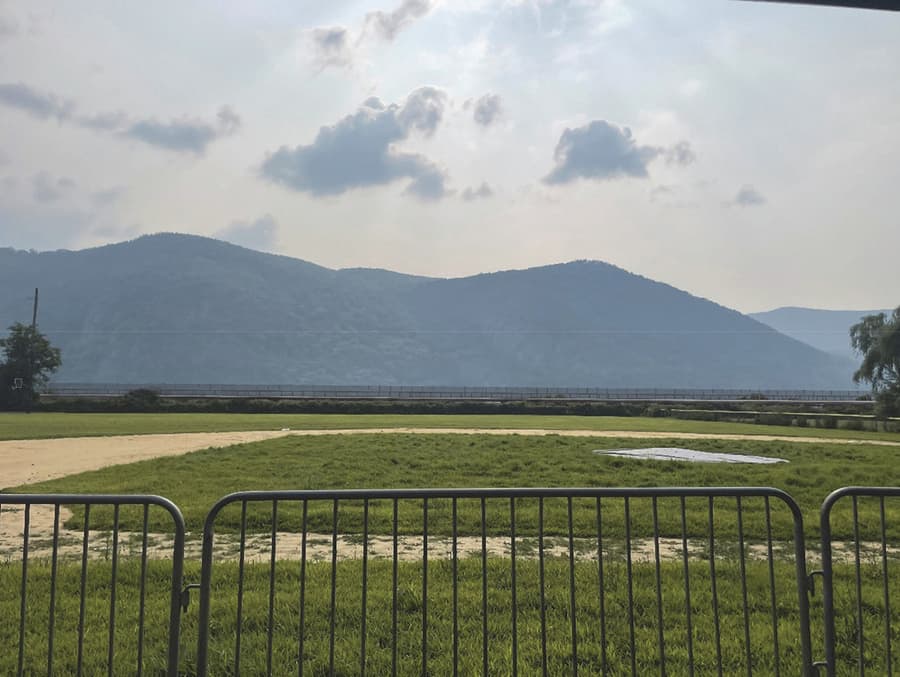 The same view west from Mayor's Park with the proposed Fjord Trail built. The elevated trail deck and its protective fence appear as a single low horizontal line running the width of the frame in front of the river, at the base of the view; the ridge and sky beyond are unchanged.