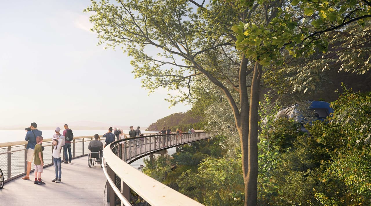 Artist's rendering of the proposed elevated shoreline trail: a broad timber-decked walkway on a gentle curve above the water, with a cable-and-post rail on the river side. Twenty or so people are spread along it: a family with two children in the foreground, a person using a manual wheelchair stopped facing the view, walkers, and a cyclist further along the curve. Mature trees lean over the deck from the landward side.