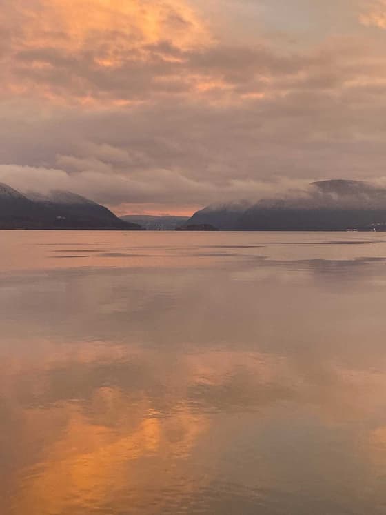 Orange and grey sunset cloud over the Hudson, the dark silhouettes of the Highlands along the horizon and the whole sky repeated in mirror-calm water.